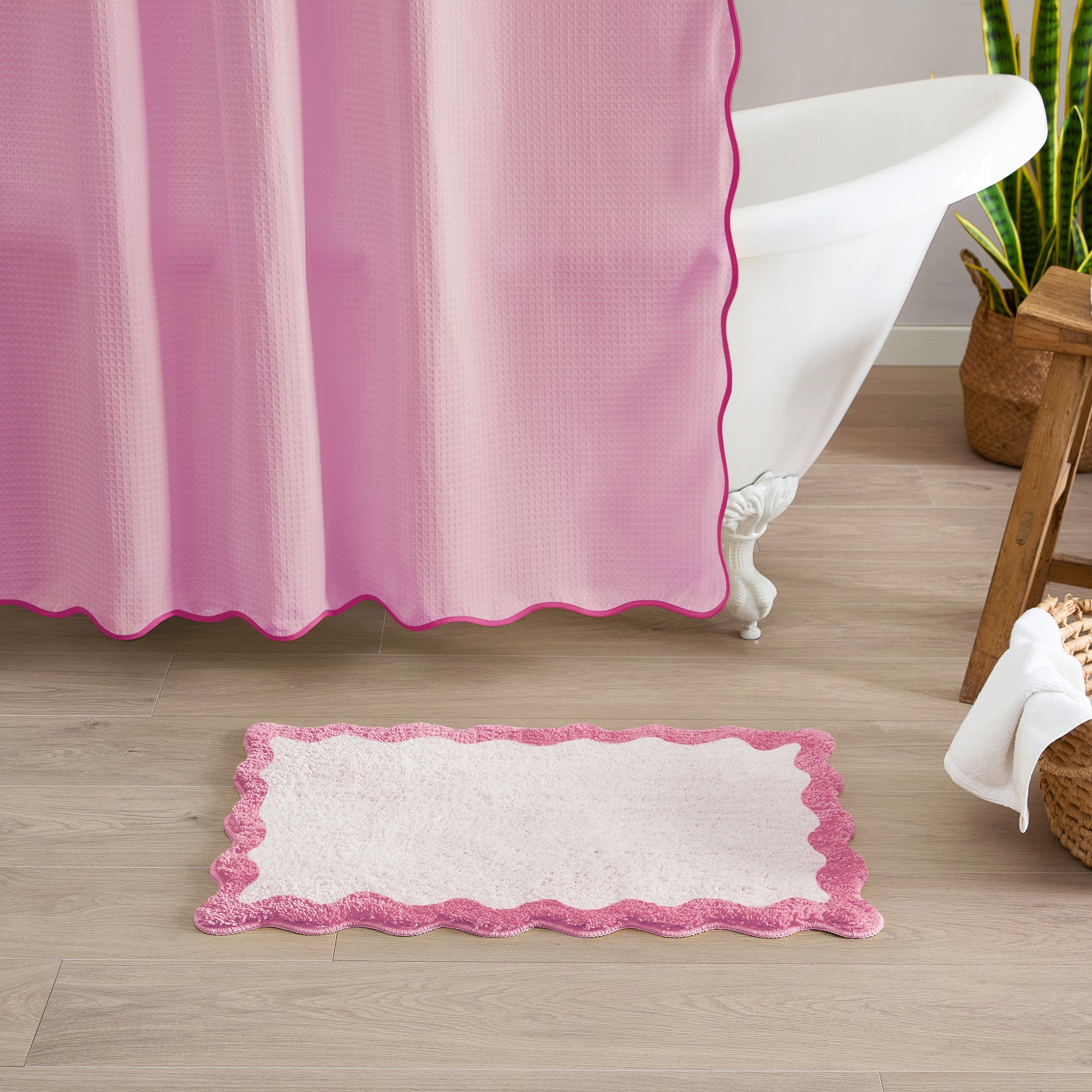 Pink and white bath mat in front of a bathtub with a pink shower curtain.