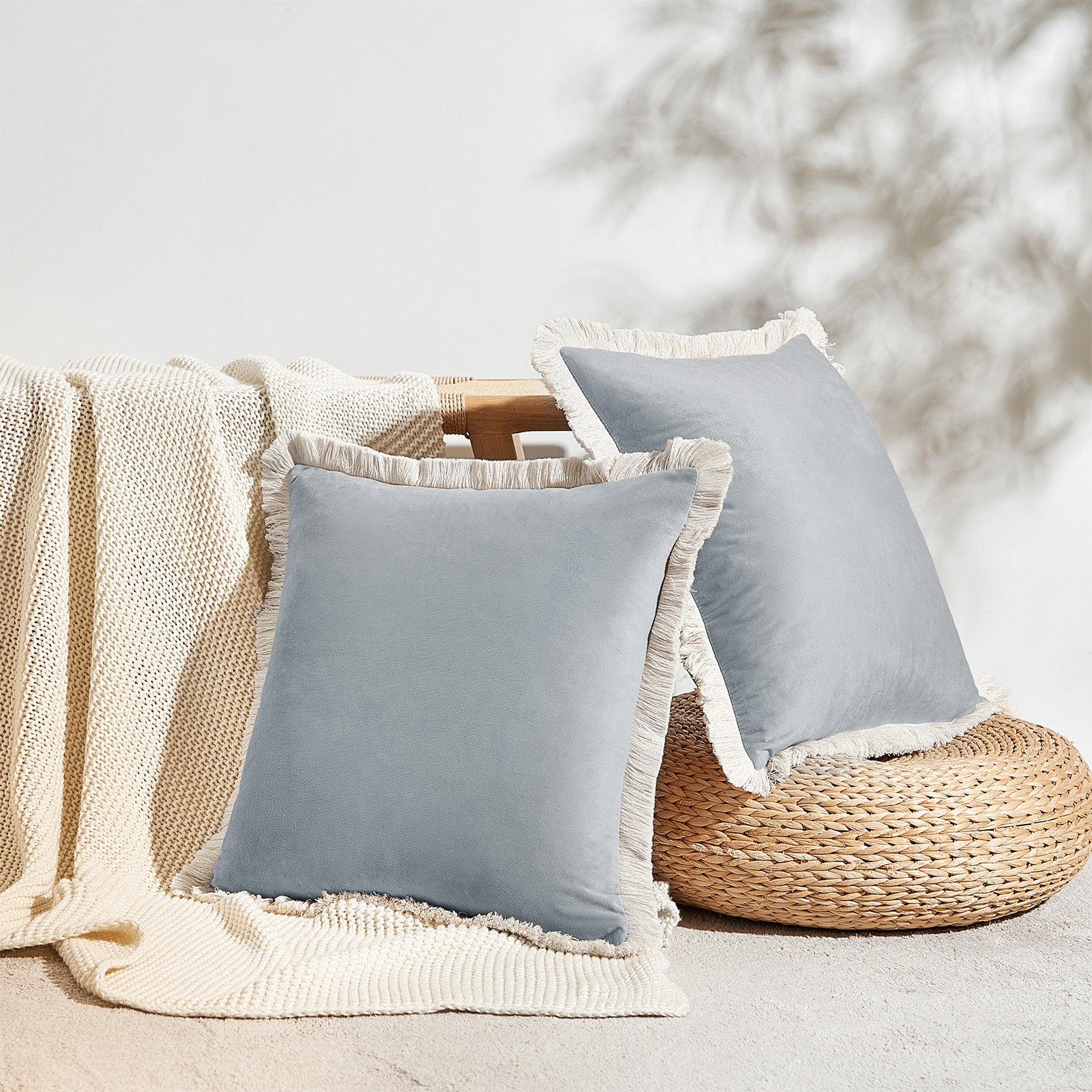 Two light blue pillows with white fringes on a textured surface with a blurred natural background