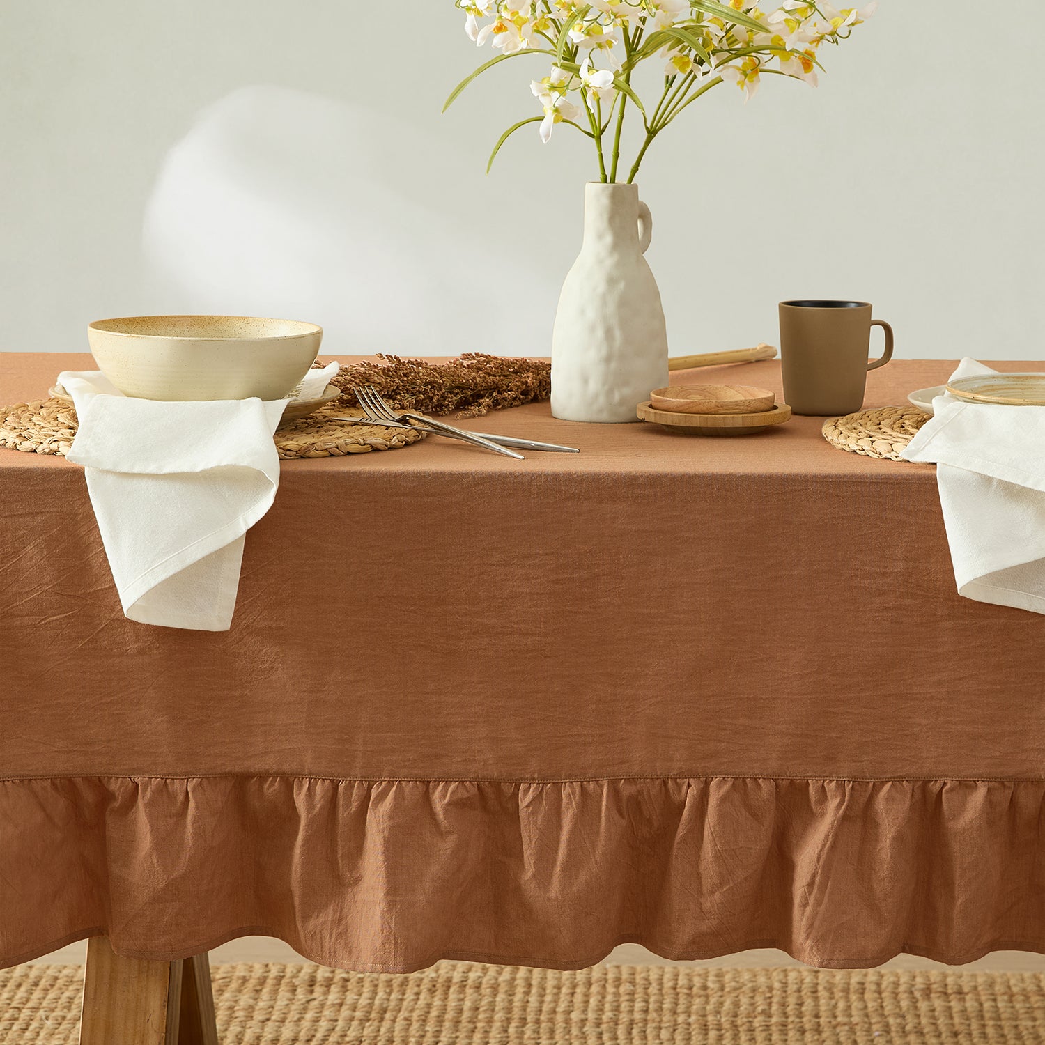 Table setting with a brown tablecloth, white vase with flowers, and ceramic items.