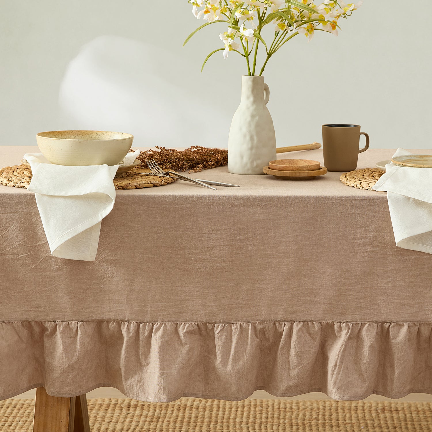 Dining table set with a beige tablecloth, ceramic plates, a vase with flowers, and a cup.