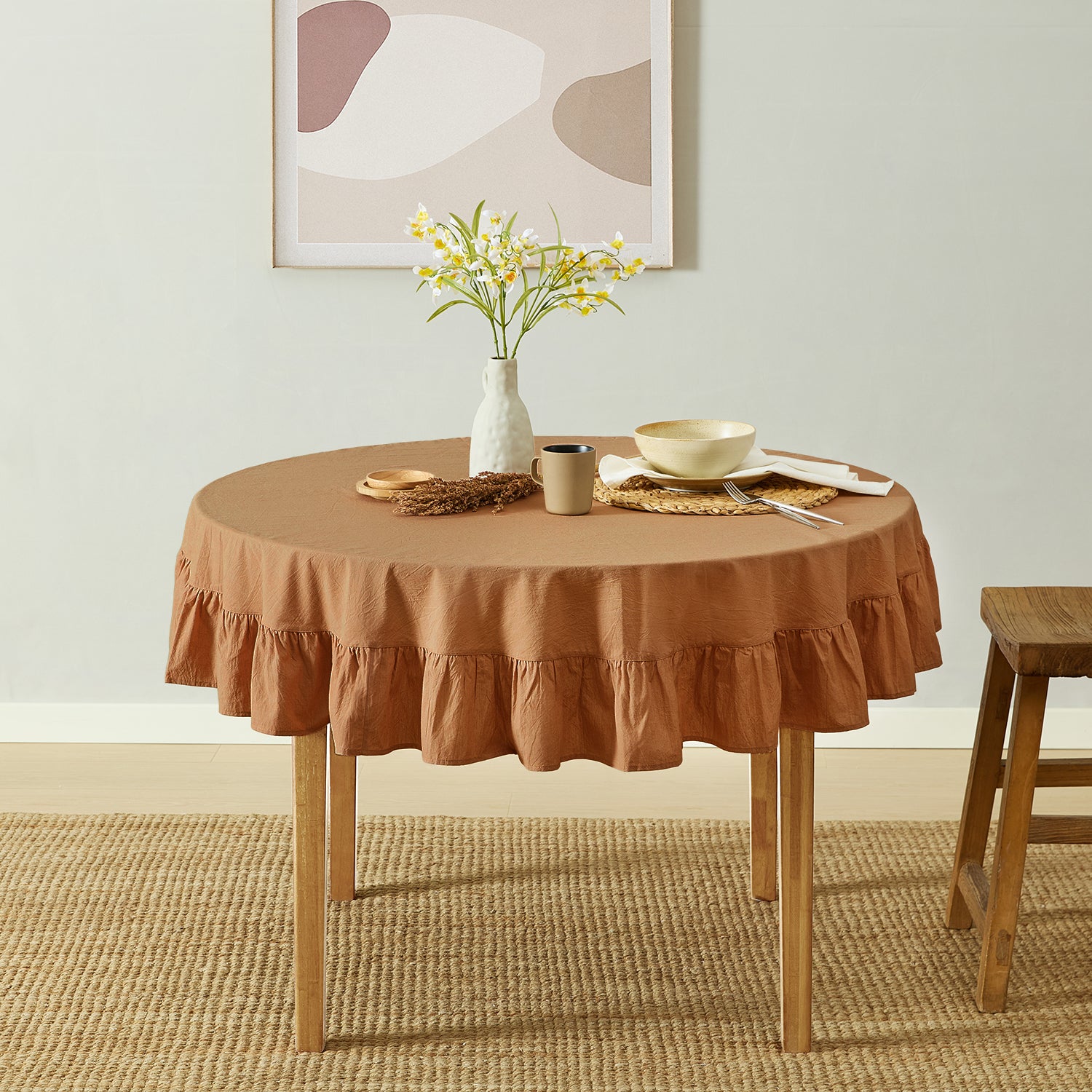 Round table with a brown ruffled tablecloth, vase with flowers, and decorative items in a room.