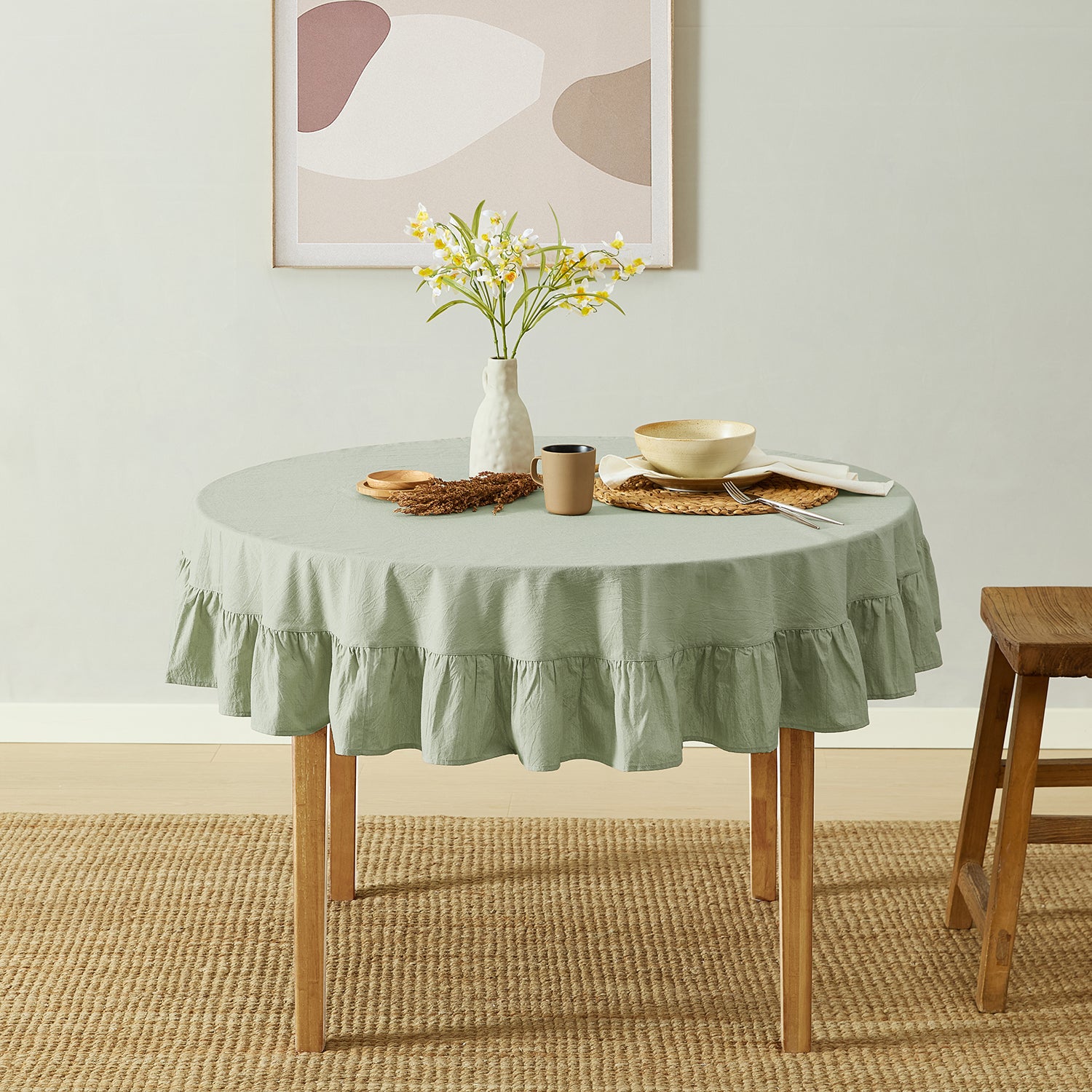 Round table with a green tablecloth, vase with flowers, and plates in a room with abstract art on the wall.