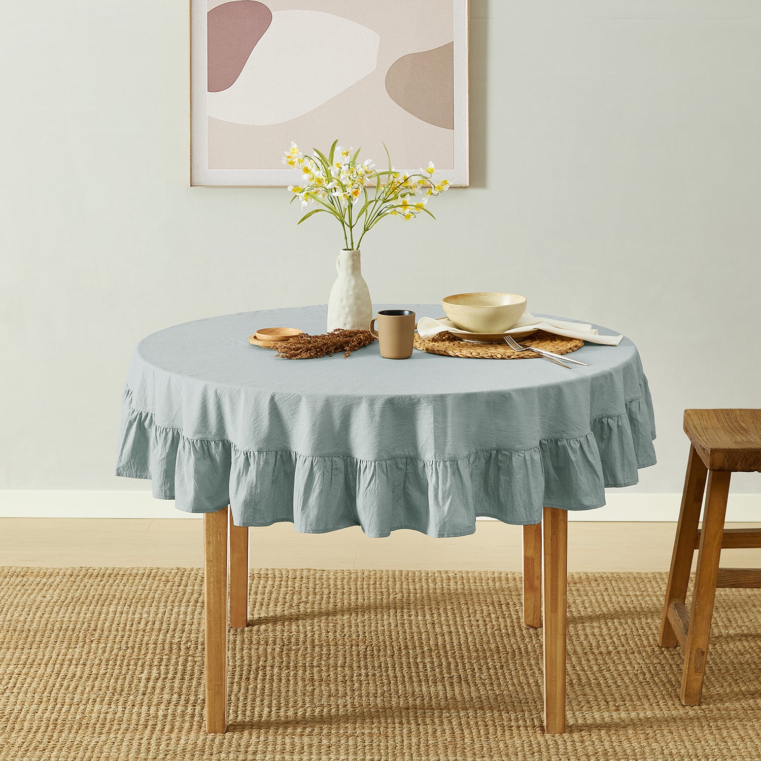Round table with a light blue tablecloth, wooden stool, and decorative items in a room.
