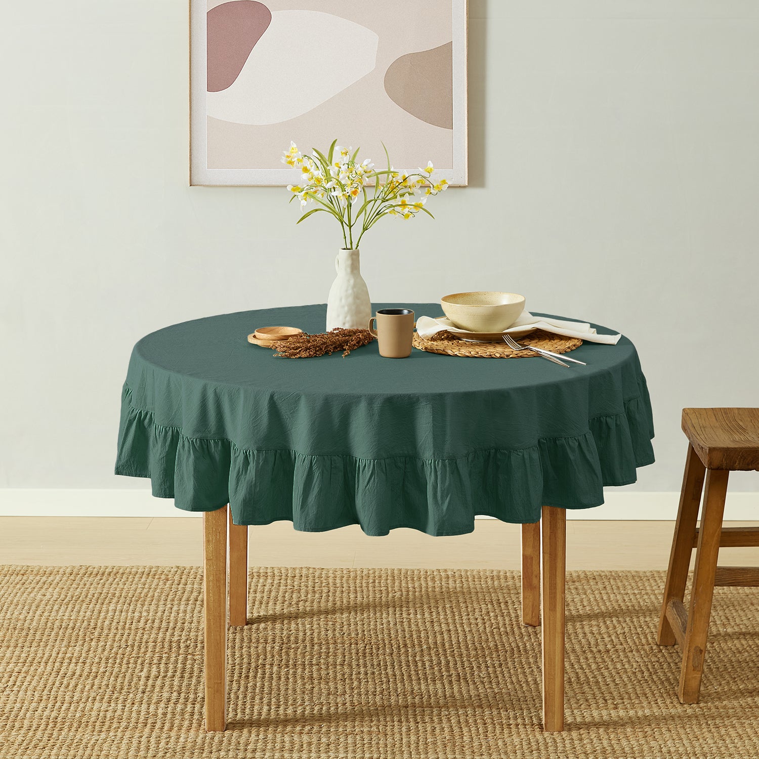 Round table with a green tablecloth in a room with a abstract painting on the wall.