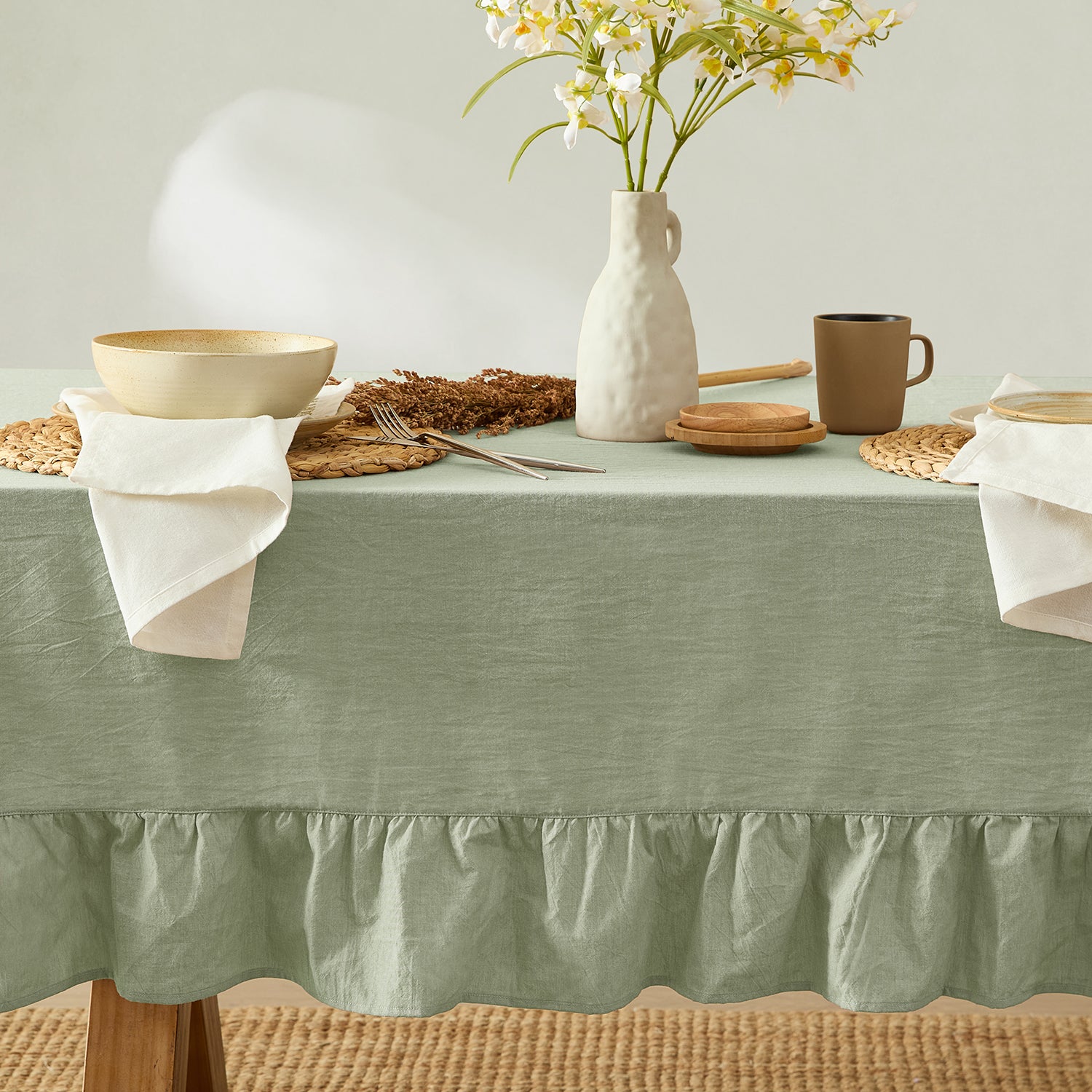Table setting with a green tablecloth, ceramic items, and flowers on a neutral background