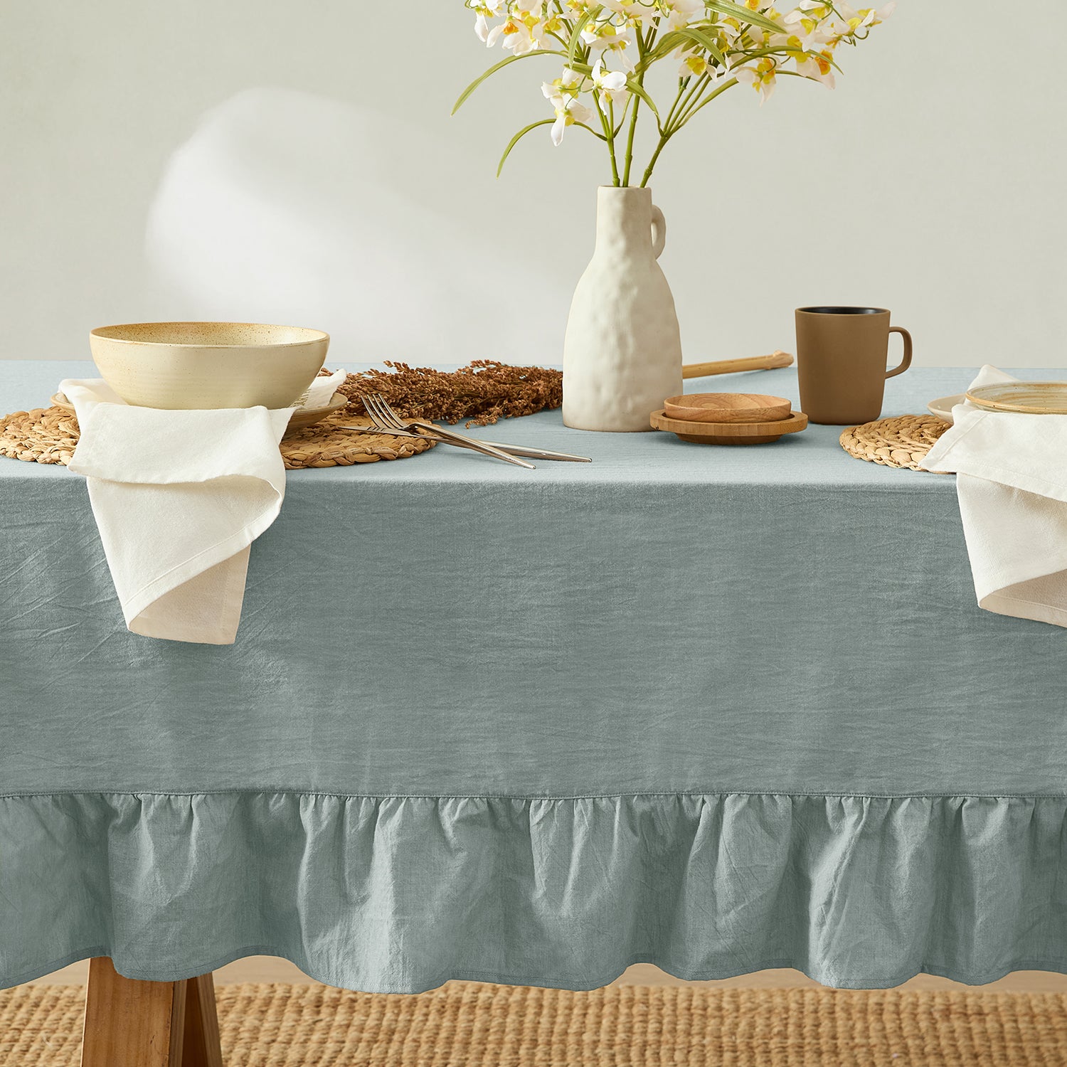 Table setting with a blue tablecloth, white plates, and a vase with flowers.