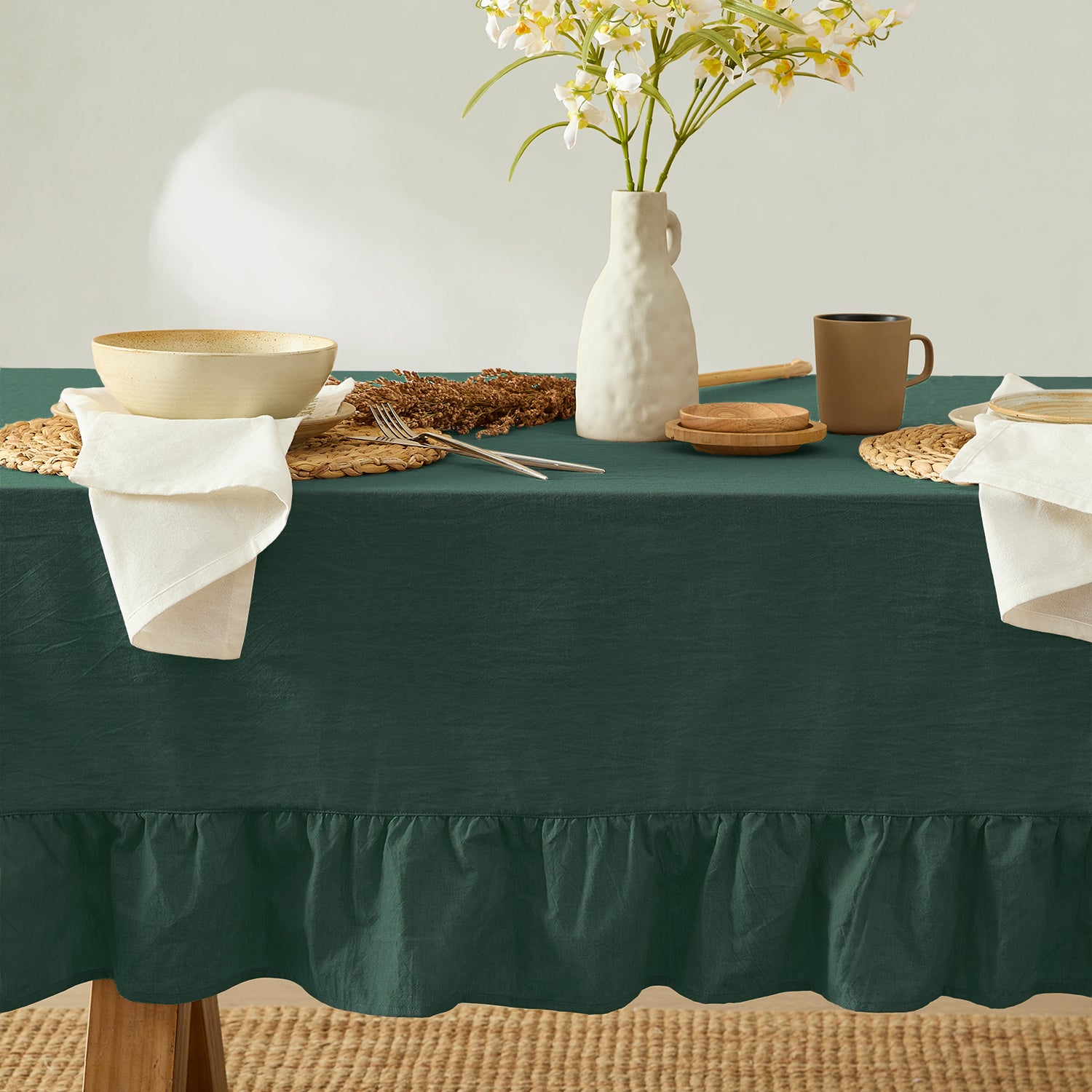 Green tablecloth with a vase of flowers, bowls, and other tableware on a wooden table.