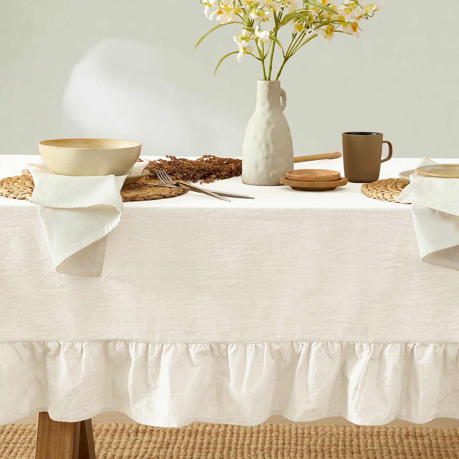 White tablecloth on a dining table with a vase of flowers, plates, and cutlery.