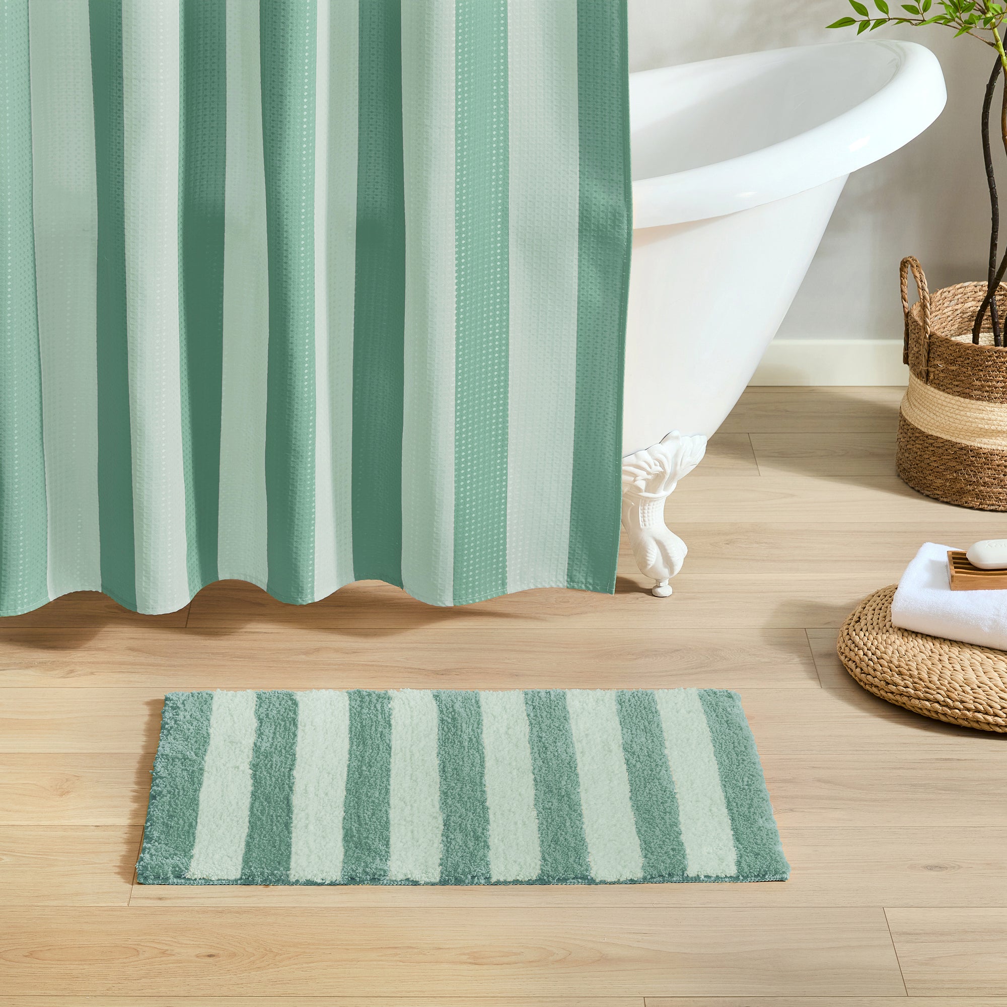 Striped shower curtain and bath mat on a wooden floor with a bathtub in the background.
