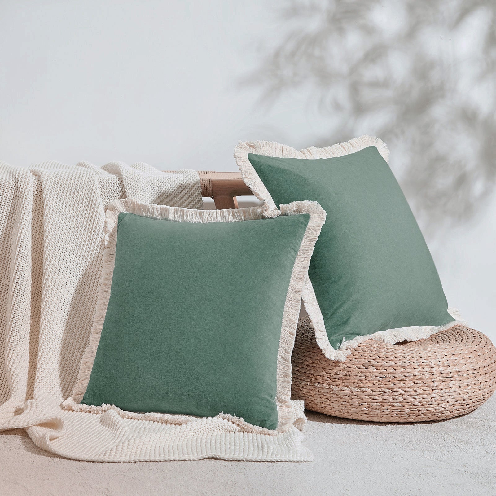 Two green pillows with white fringes on a neutral background