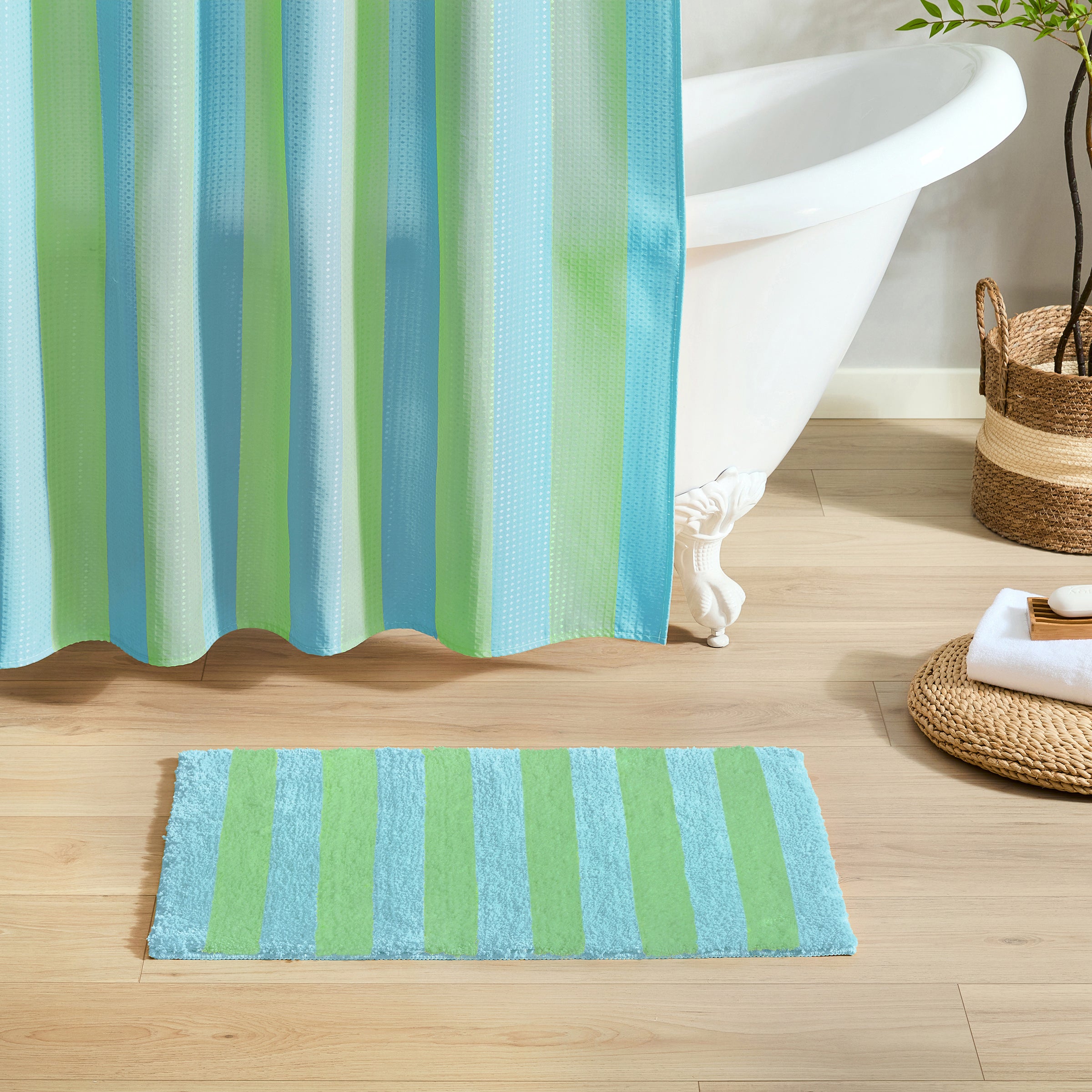 Striped shower curtain and bath mat on a wooden floor with a bathtub in the background.