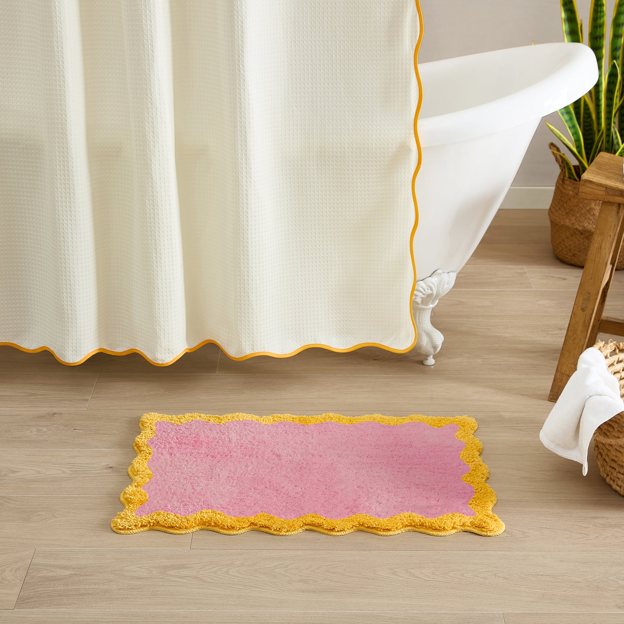 Pink bath mat with yellow trim on a wooden floor next to a bathtub.