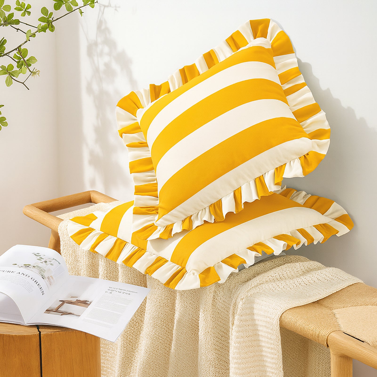 Yellow and white striped cushions on a wooden stool with a book and plant in the background.