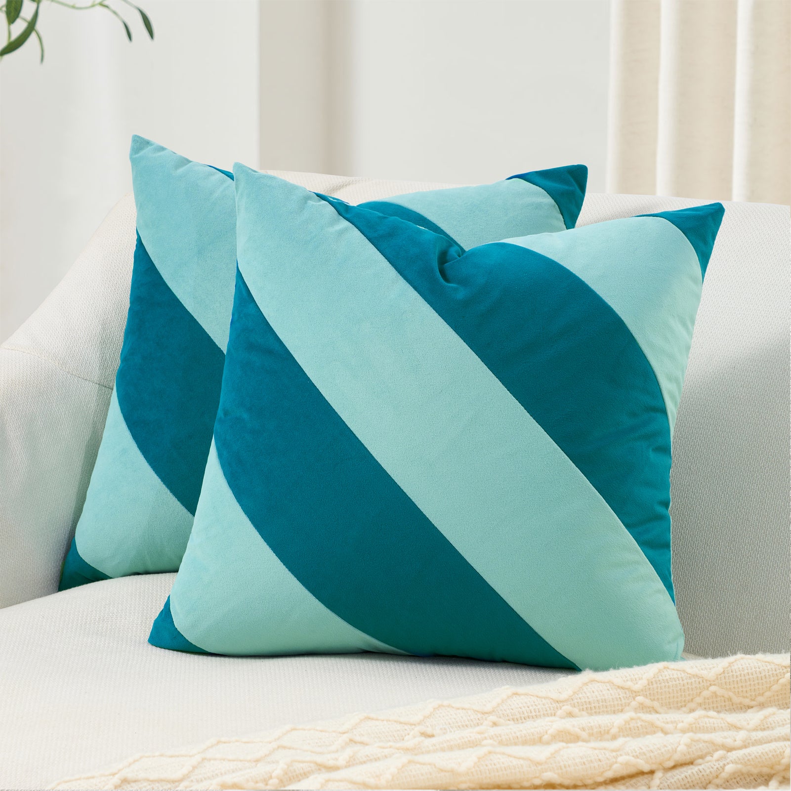 Two blue and green striped pillows on a white couch.