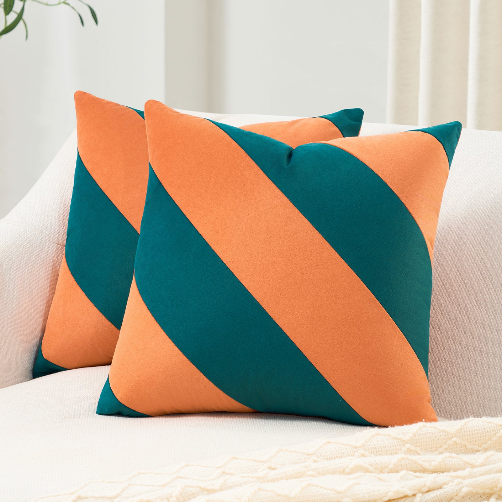 Two orange and teal striped pillows on a white couch.