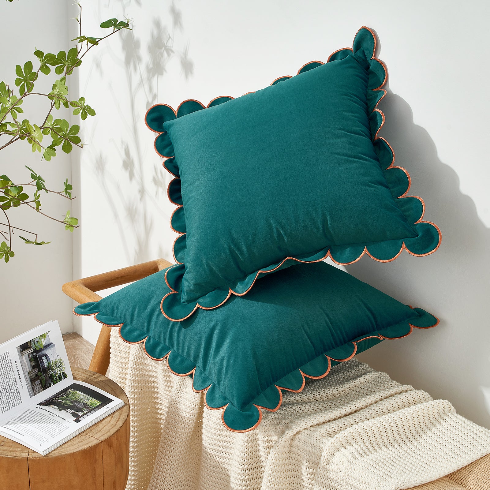 Teal cushions with scalloped edges on a chair next to a plant and open book.