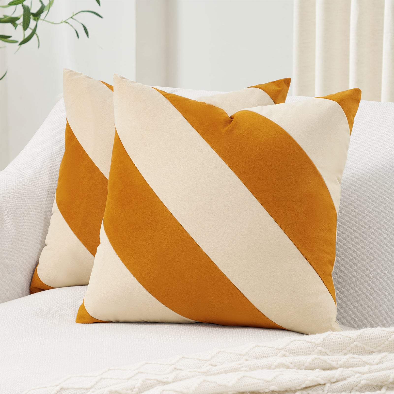 Two orange and white striped pillows on a white couch with a neutral background