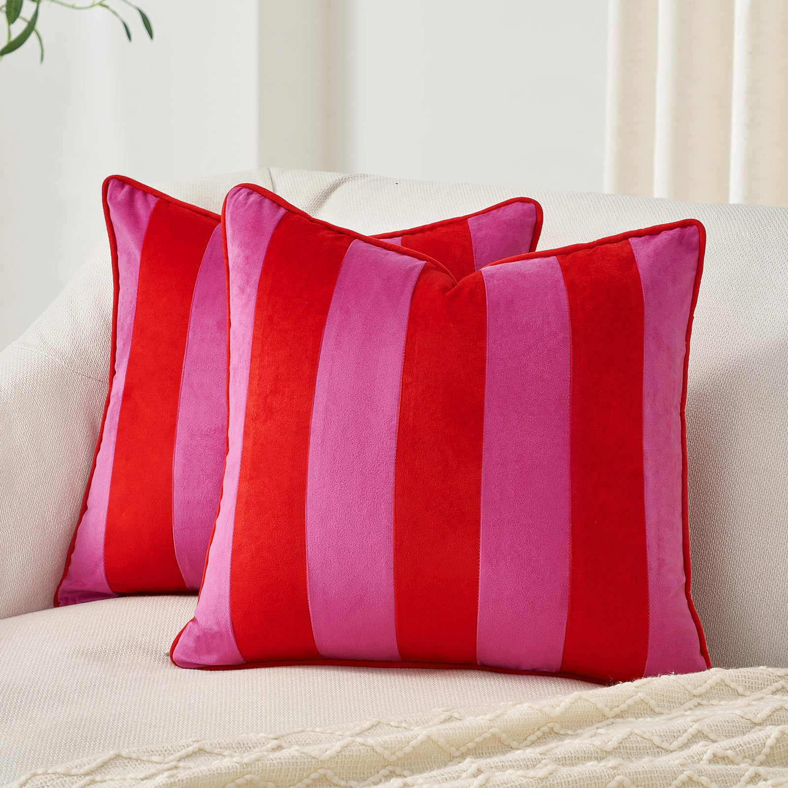 Two red and pink striped pillows on a white couch.