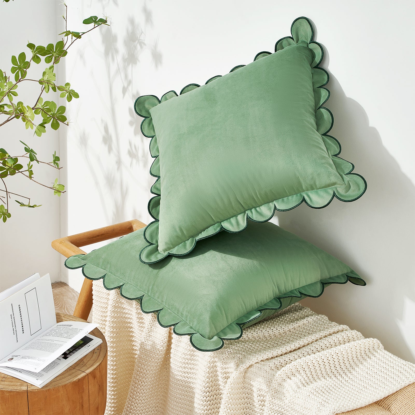 Two green pillows with scalloped edges on a wooden stool against a white wall.