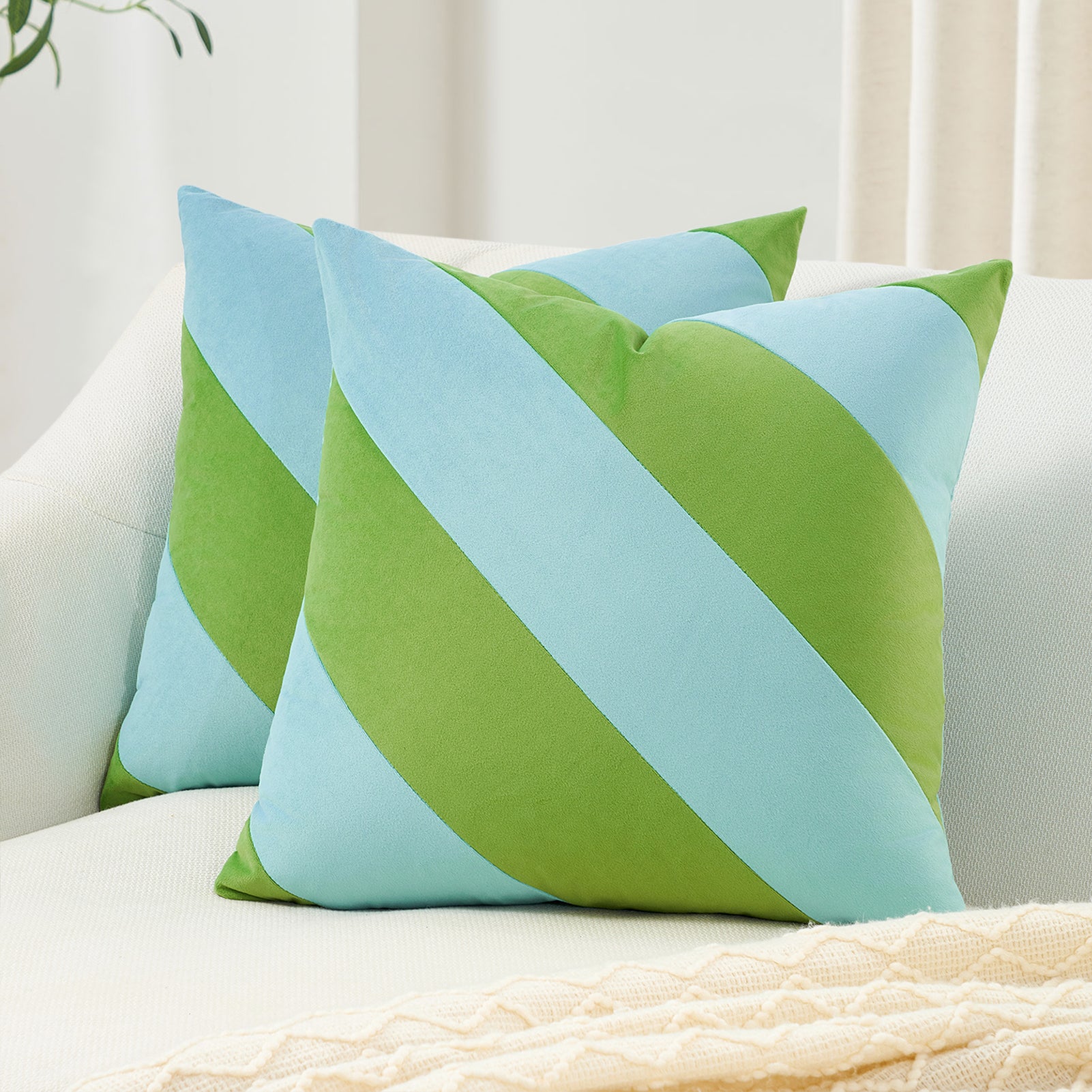 Two green and light blue striped pillows on a white couch.
