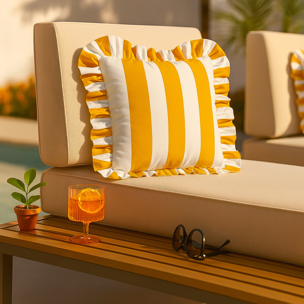 Beige outdoor sofa with yellow and white striped cushions, a glass of orange juice, and sunglasses on a wooden table.