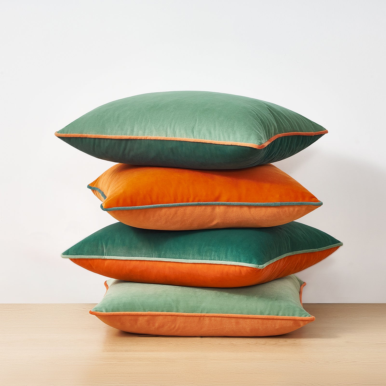 Stack of green and orange cushions on a wooden surface with a light gray background
