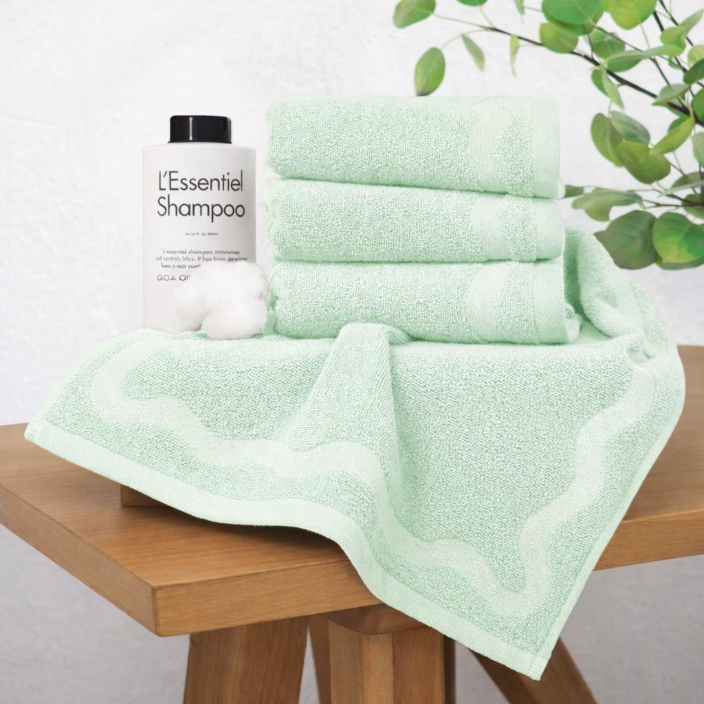 Green towels and shampoo bottle on a wooden surface with a plant in the background