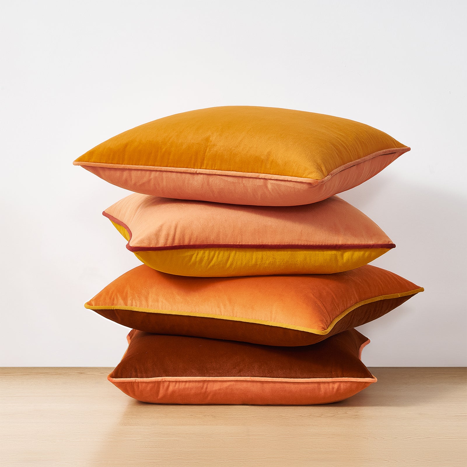 Stack of orange pillows on a light wooden surface with a white background