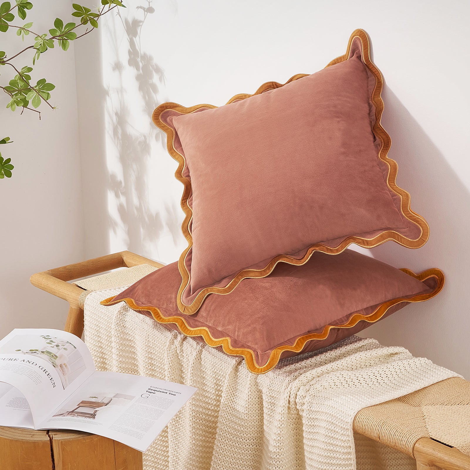Pink velvet pillows with scalloped edges on a wooden bench with a white blanket and open book.