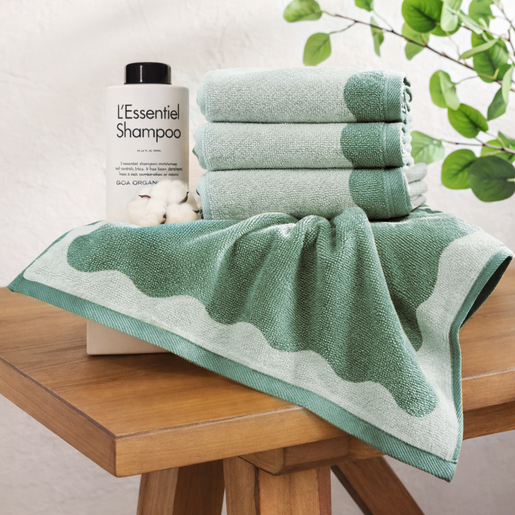 Green towels on a wooden table with a bottle of shampoo in the background