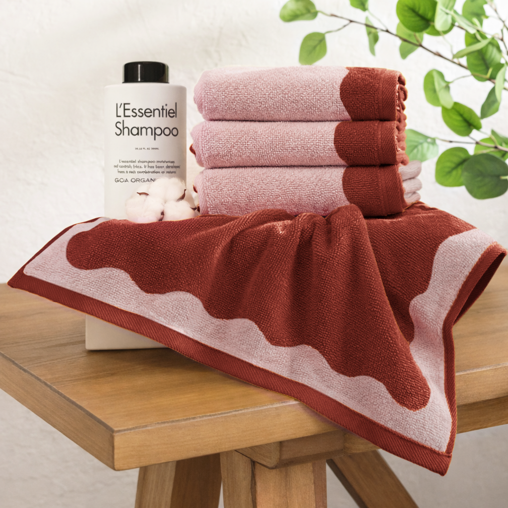 Red and pink towels on a wooden table with a bottle of shampoo in the background.