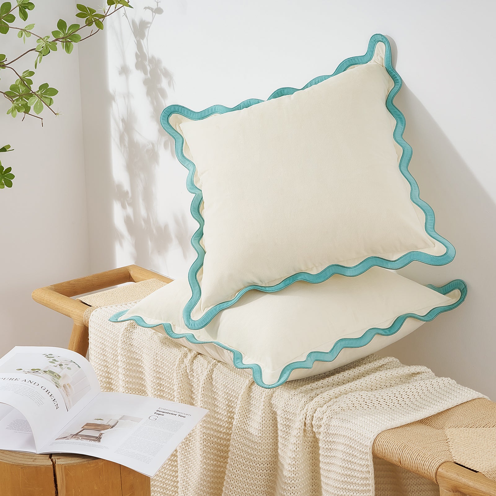 Decorative pillow with turquoise edge on a wooden stool with a blanket and book.