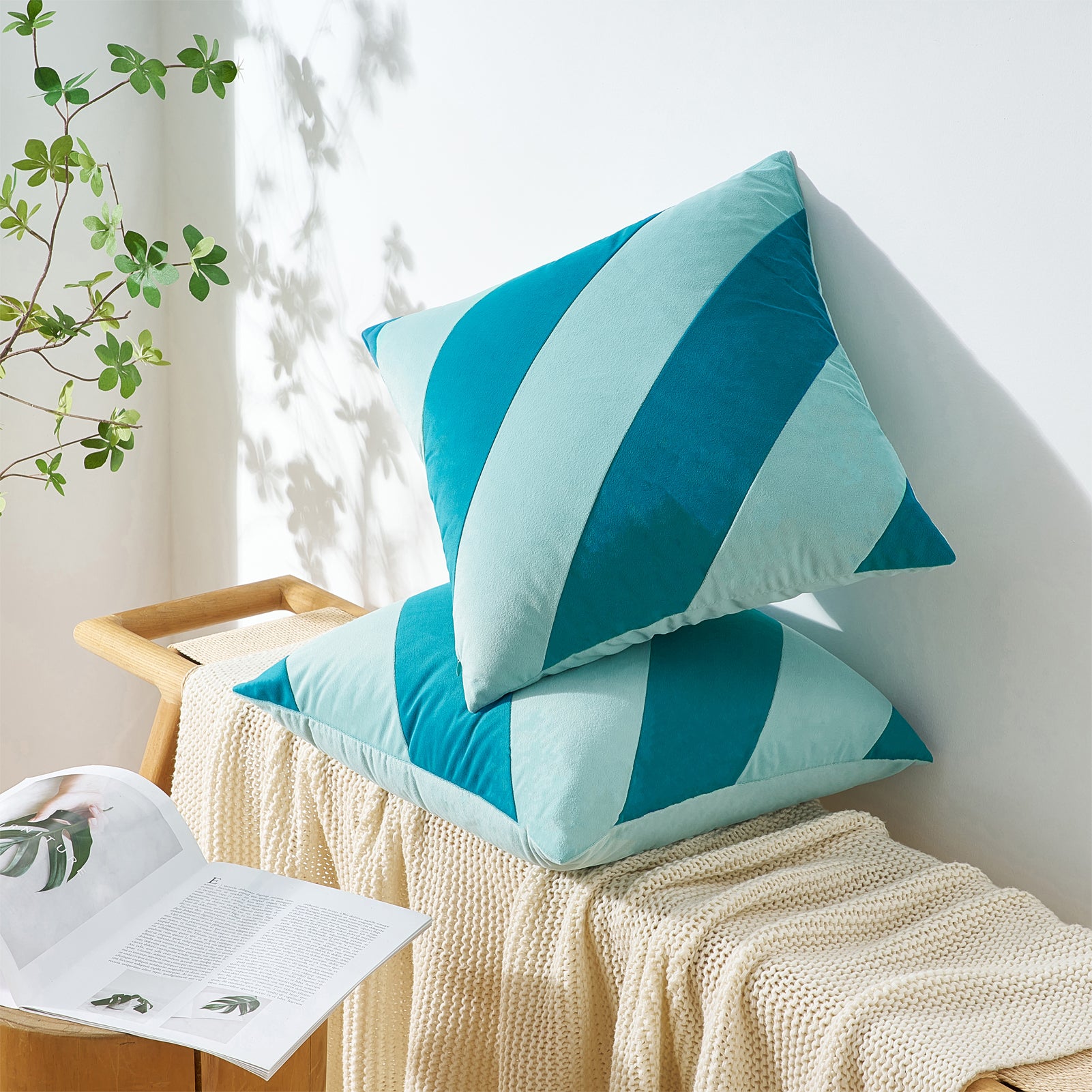 Teal and light blue striped cushions on a white surface with a plant in the background
