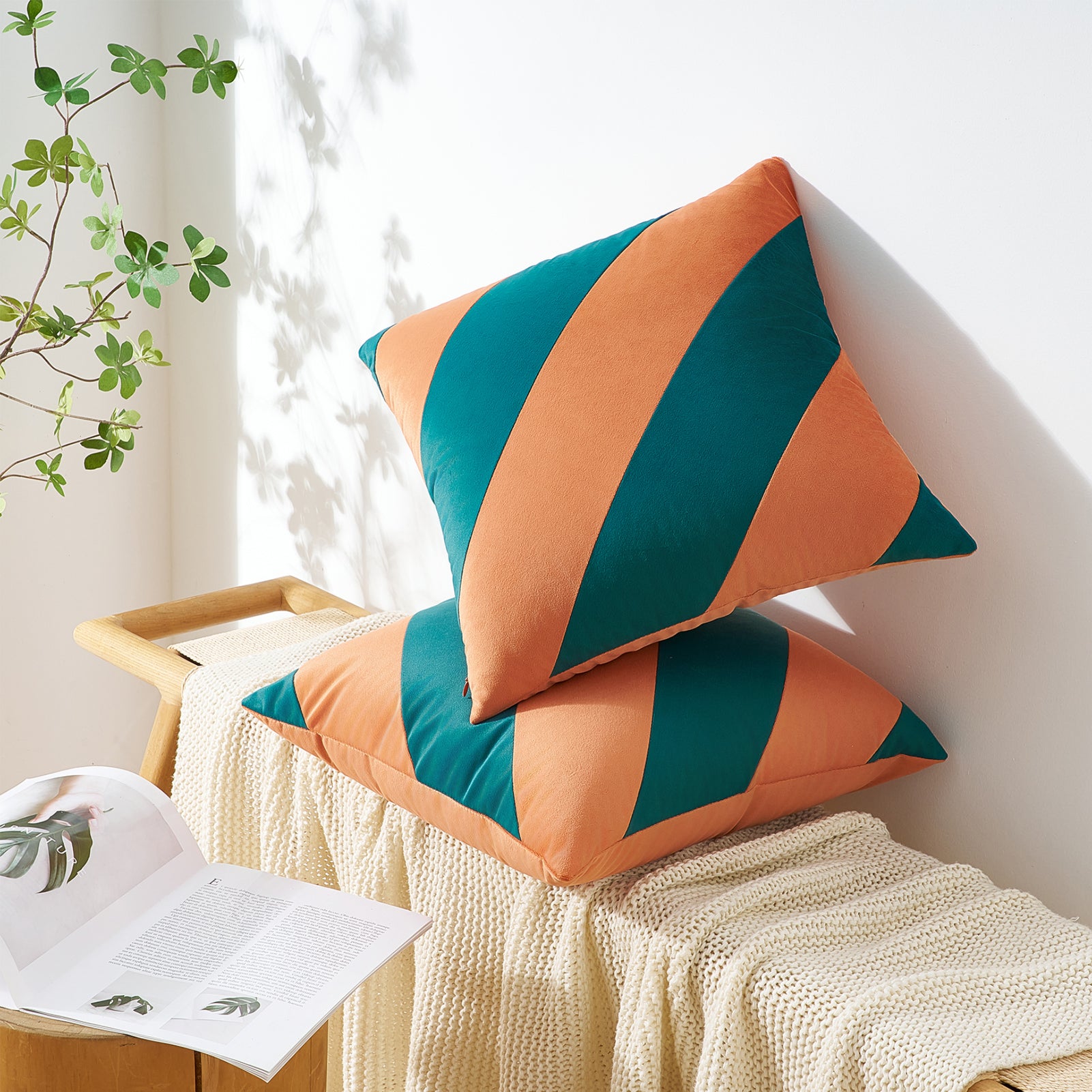 Two striped orange and green cushions on a white surface with a plant in the background
