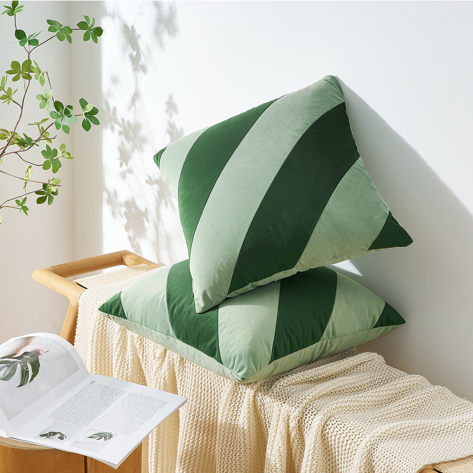 Green and white striped pillows on a bench with a plant and magazine in the background