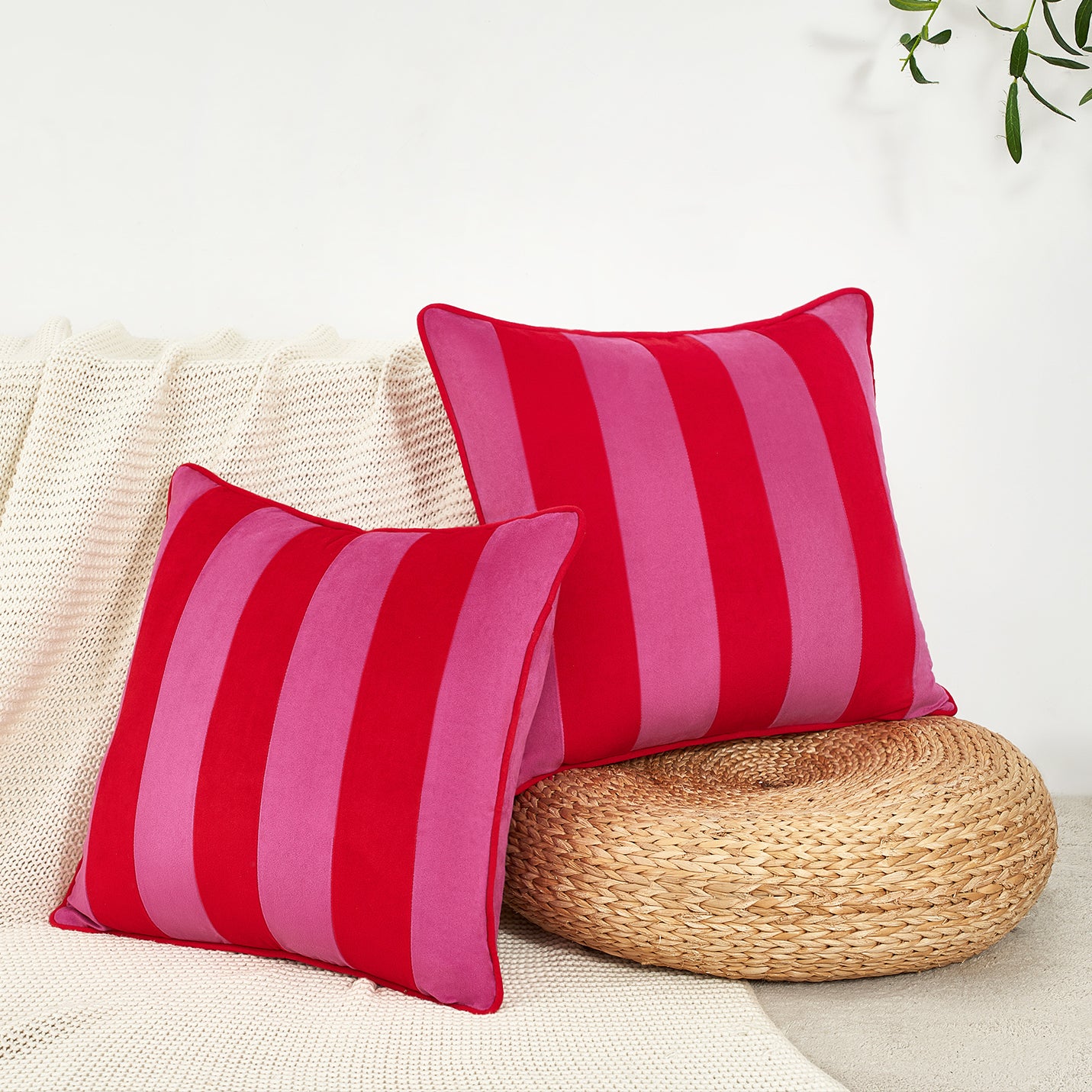 Two red and pink striped pillows on a beige couch with a woven round pillow.