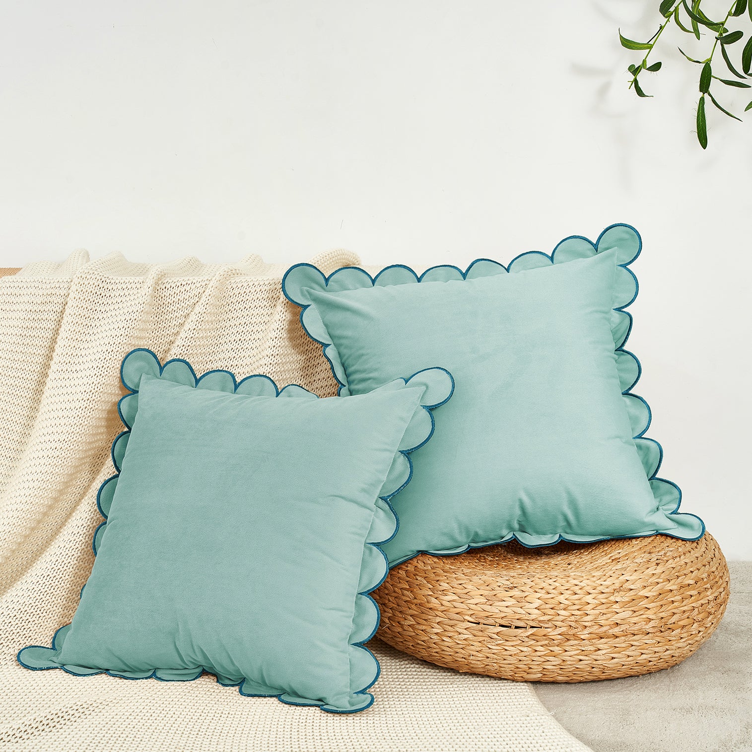 Two light blue pillows with scalloped edges on a woven stool against a neutral background.