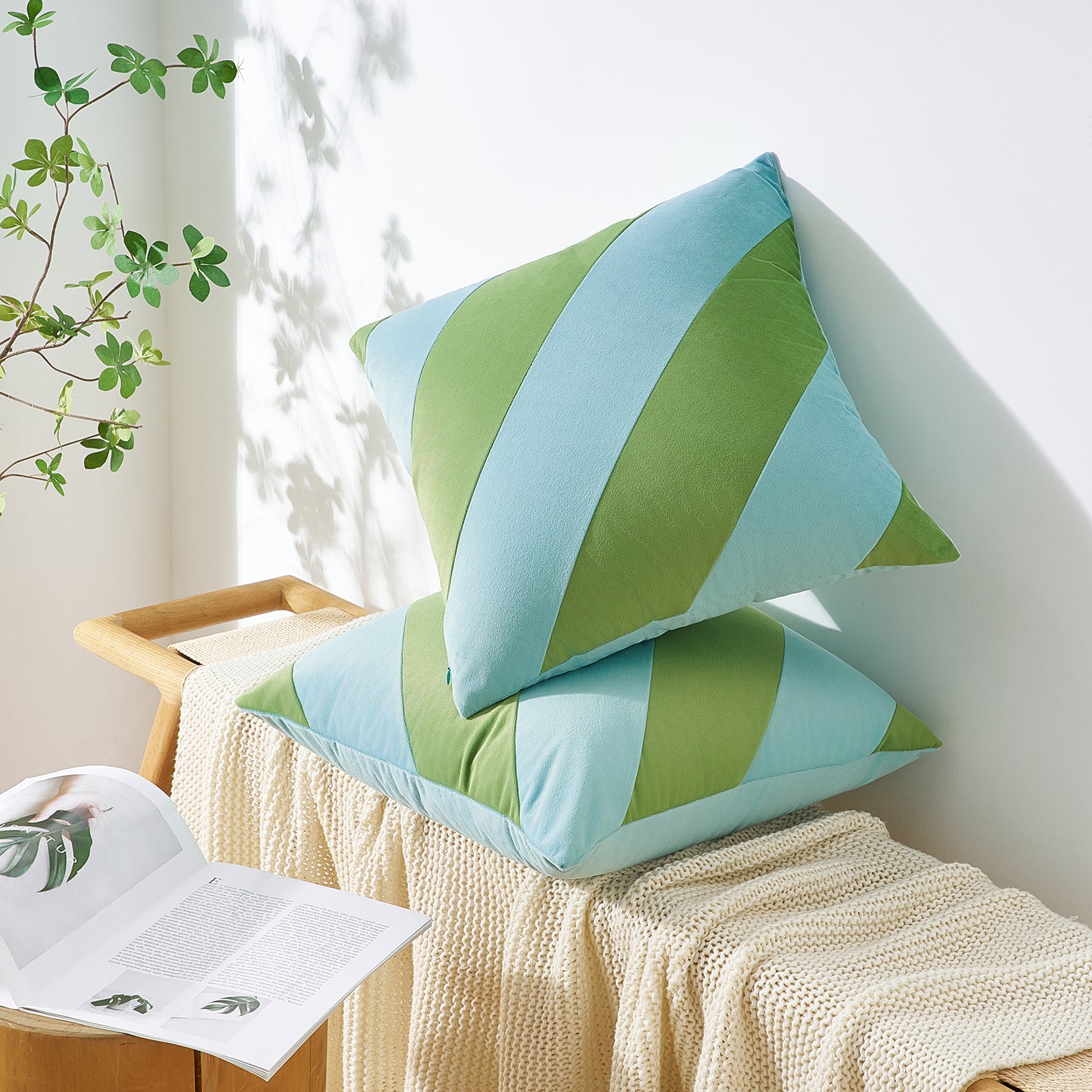 Green and blue striped pillows on a white surface with a plant in the background