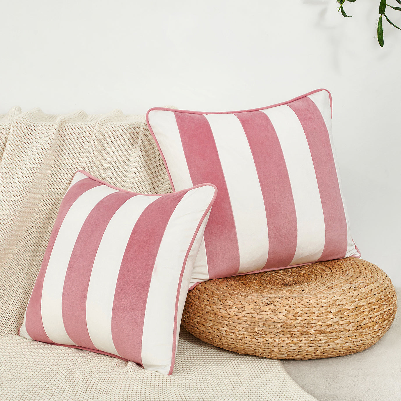 Pink and white striped pillows on a beige couch with a woven round pillow.