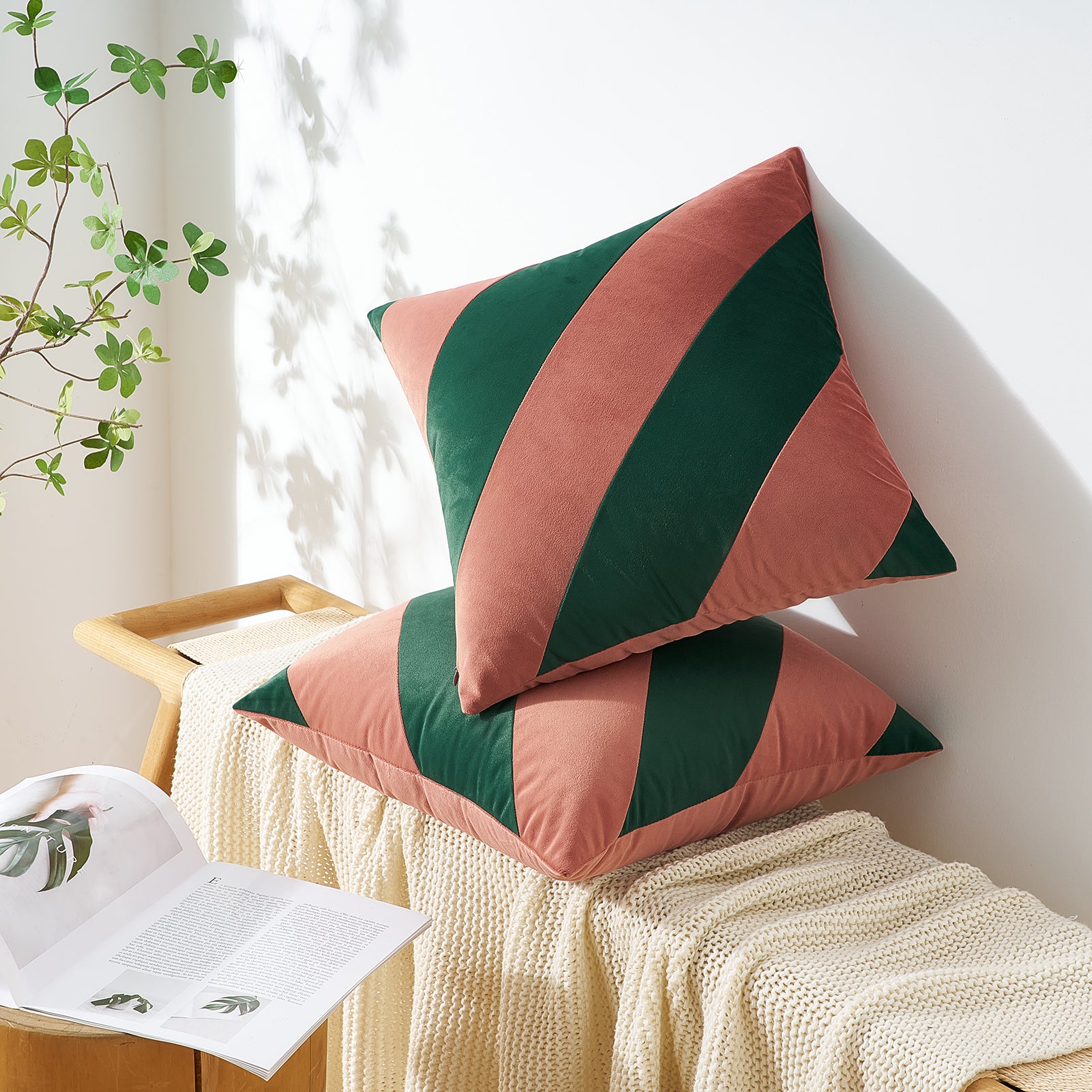Two pink and green patterned pillows on a white surface with a plant in the background.