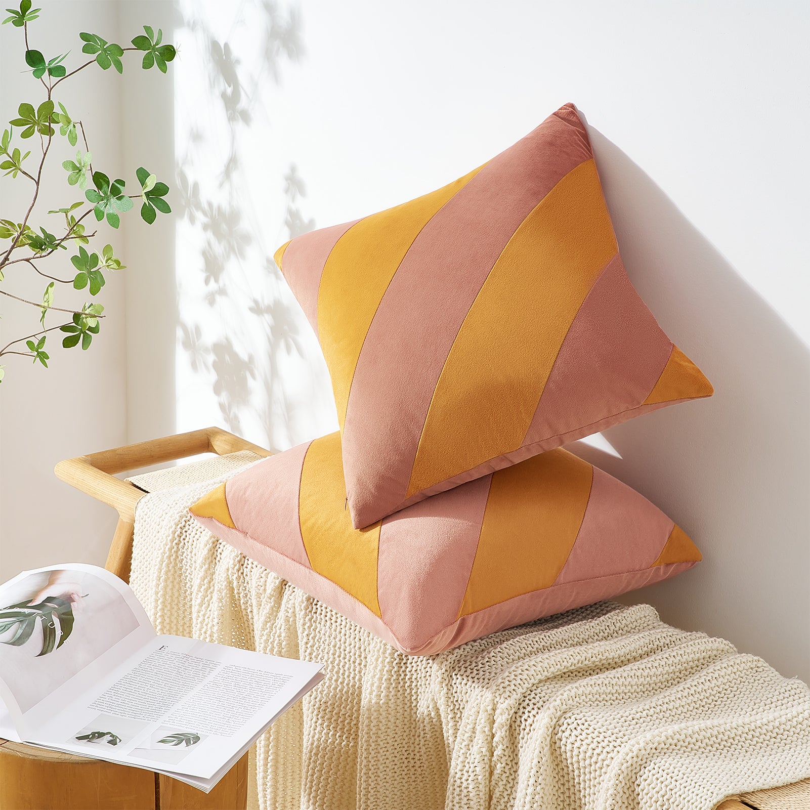 Two colorful pillows on a bench with a plant and book in the background