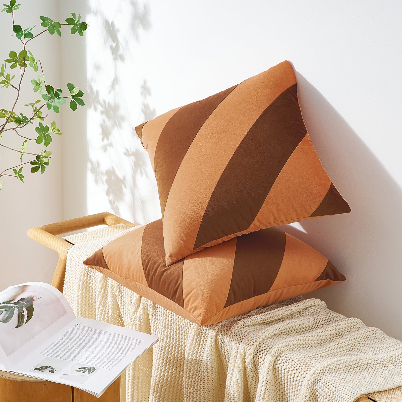 Two brown striped pillows on a white surface with a plant in the background