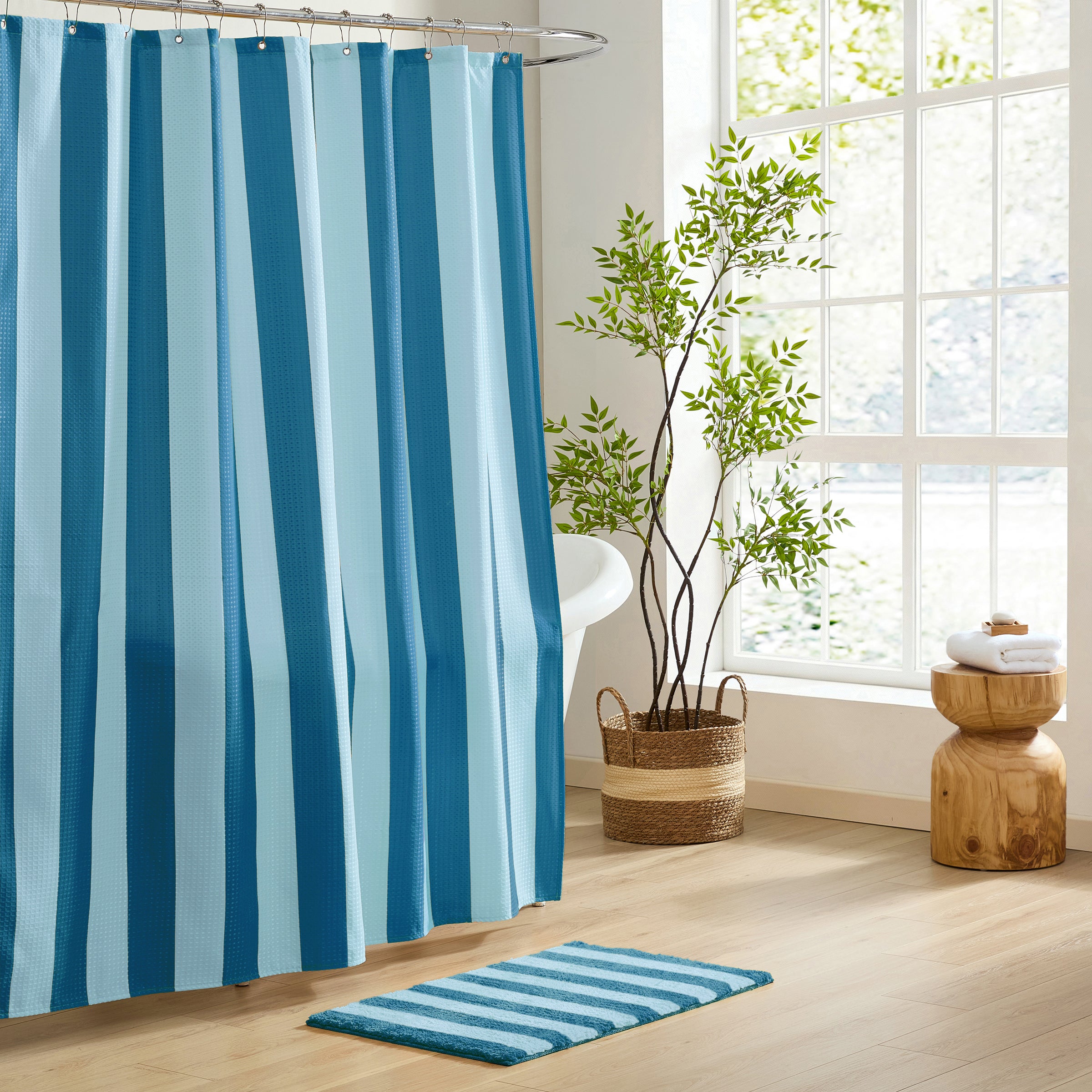 Bathroom with blue and white striped shower curtain and rug, plant, and wooden stool.