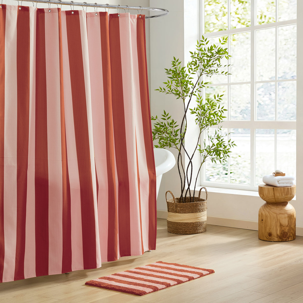 Striped shower curtain and rug in a bathroom with a plant and wooden stool.