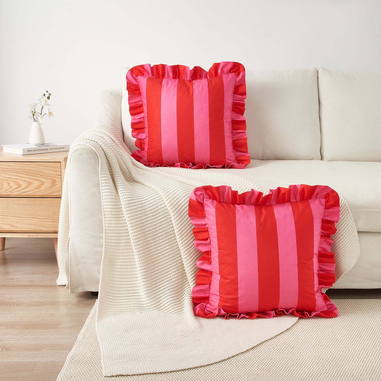 Two red and pink striped pillows on a beige sofa with a wooden side table in the background.