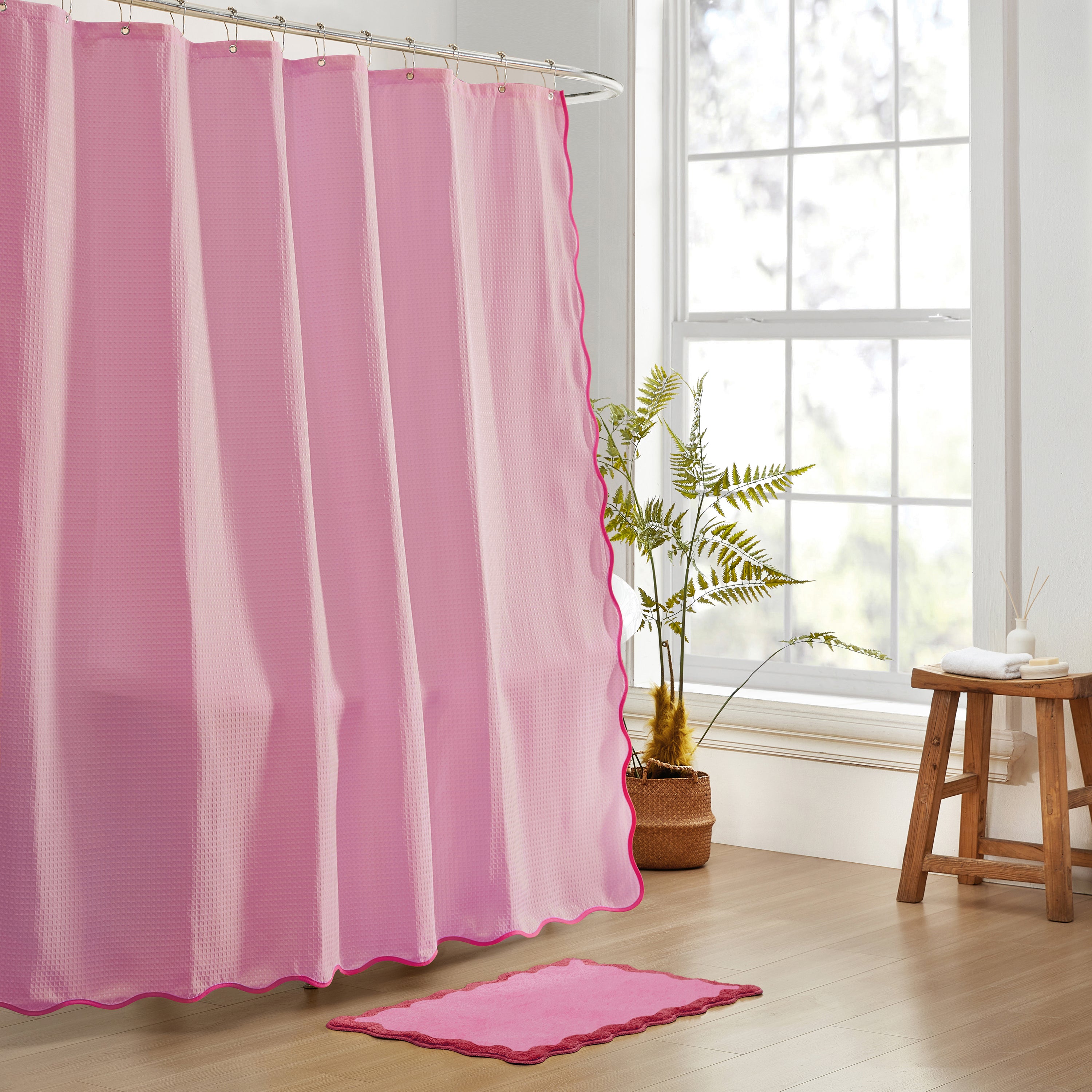 Pink shower curtain and rug in a bathroom with a window and stool.