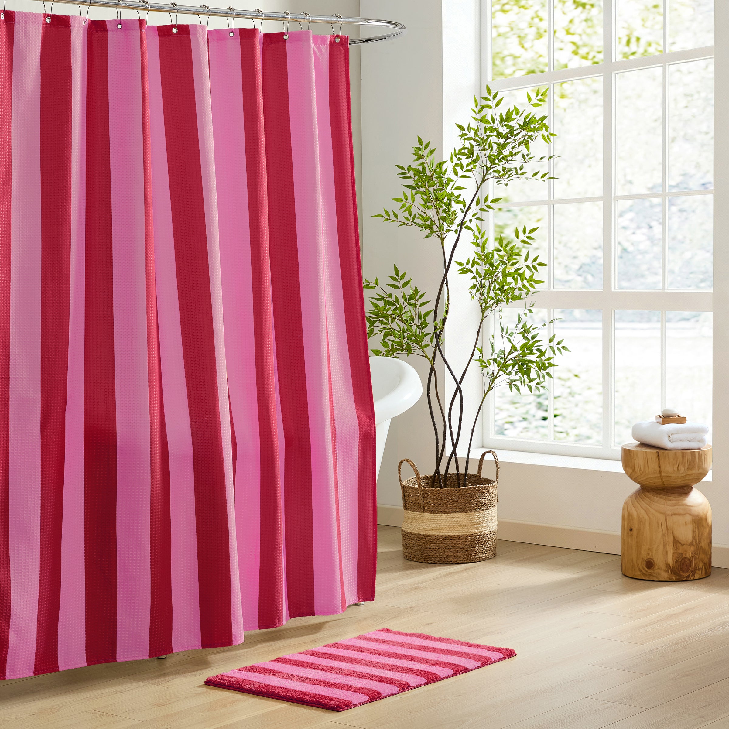 Bathroom with pink and red striped shower curtain and matching rug, plant, and wooden stool.