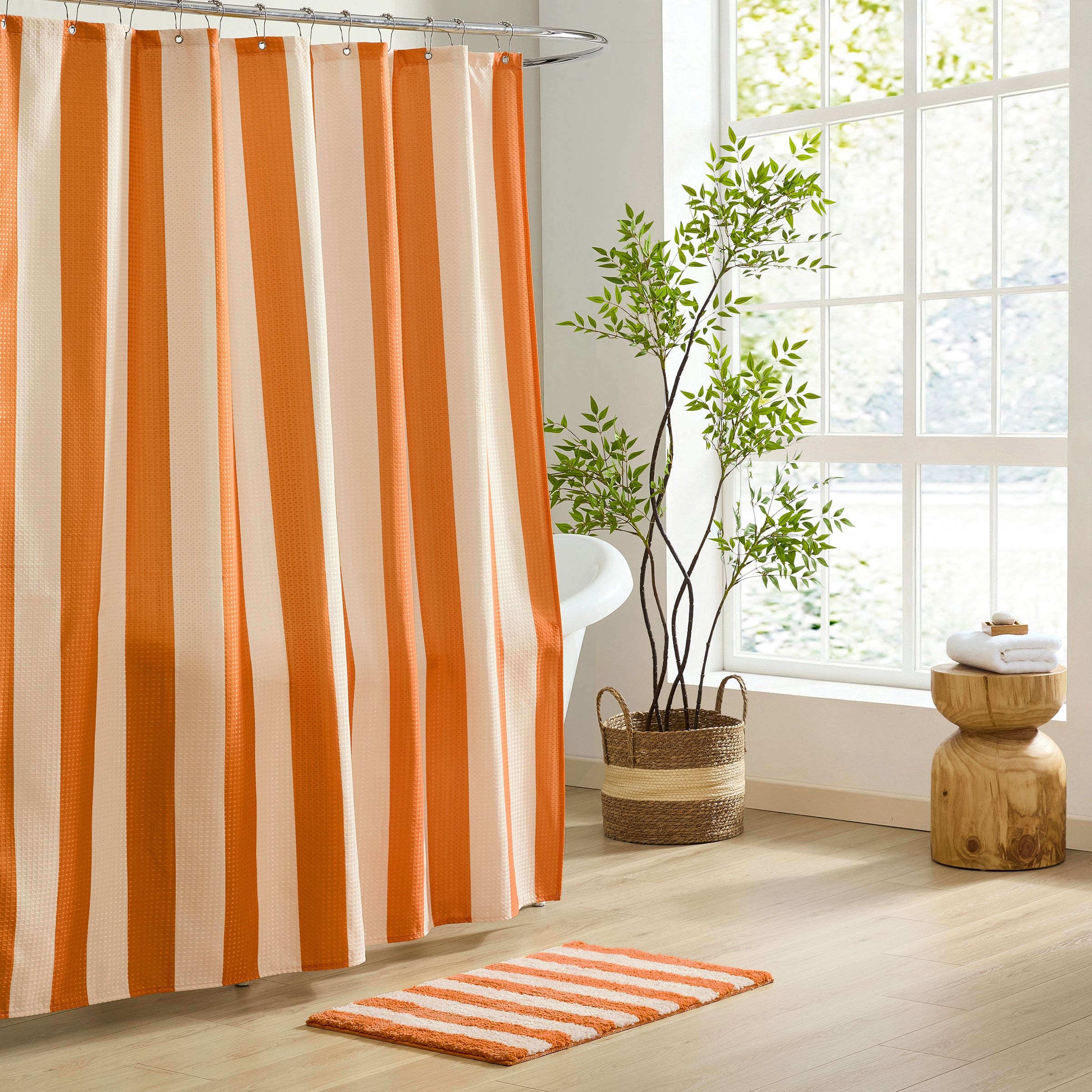 Bathroom with orange and beige striped shower curtain and rug, plant, and wooden stool.