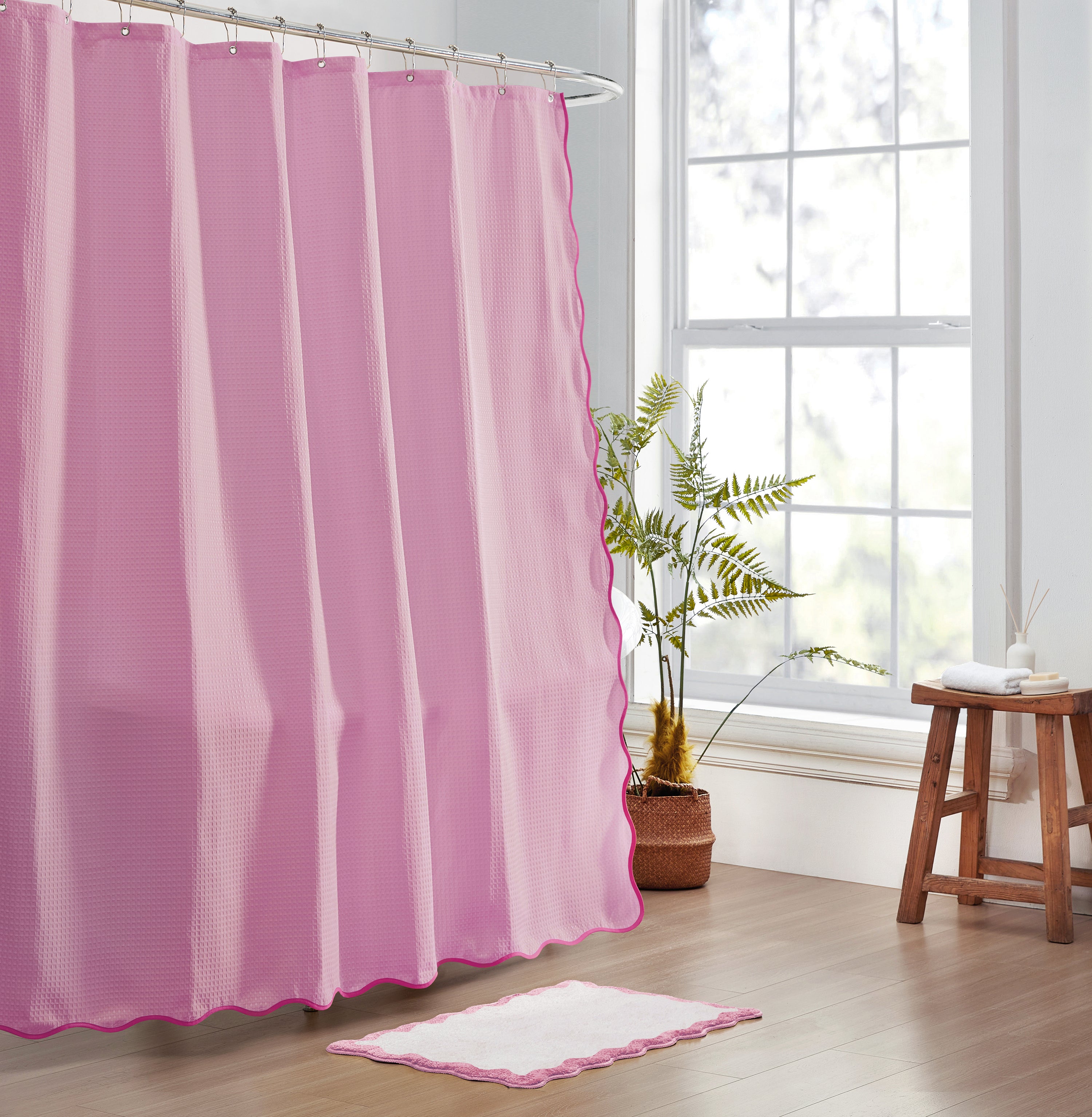 Pink shower curtain in a bathroom with a window and plant in the background