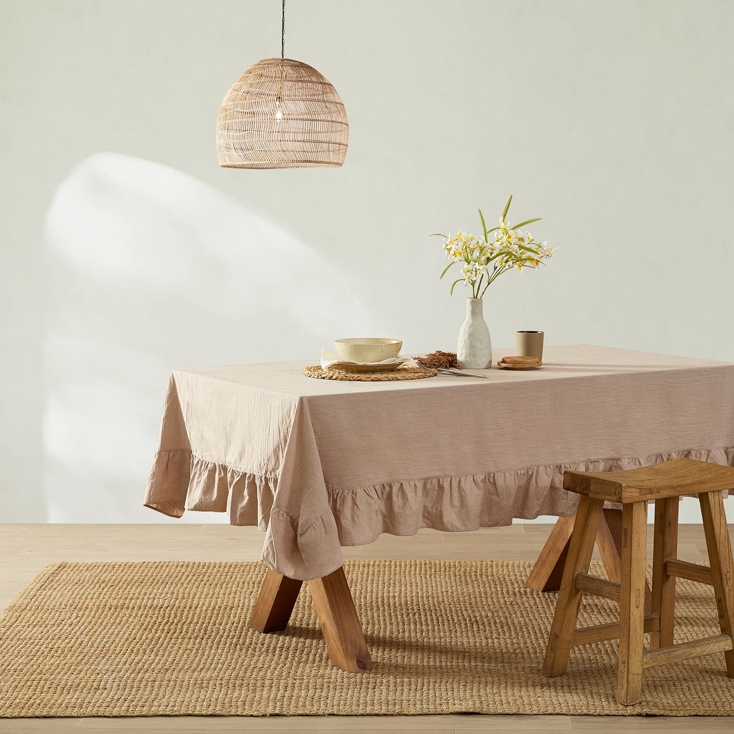 Dining room with a table covered by a beige tablecloth, wooden stool, and decorative elements.